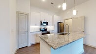 This single-floor residence offers a thoughtfully designed open-concept layout finished with contemporary details throughout. The kitchen serves as a central highlight, showcasing a large island with granite countertops and an undermount sink, white shaker-style cabinetry, a textured tile backsplash, and a full suite of stainless steel appliances including a range, microwave, dishwasher, and refrigerator. Pendant lighting above the island adds a refined touch, while wood-look flooring extends seamlessly into the surrounding living areas.

The living space is bright and airy, benefiting from multiple windows and a ceiling fan overhead. A private entry door with transom window allows additional natural light to filter in. An additional room provides flexible use, enhanced by a built-in desk with granite surface and open shelving—ideal as a home office or study nook.

Bedrooms are generously proportioned with large windows offering outdoor views and ample natural light. The primary bathroom is elegantly appointed with marble-look tile flooring, a dual-sink vanity with granite countertops, blue-grey cabinetry, and a frameless glass walk-in shower with full-height marble tile surround. The overall aesthetic is clean, modern, and cohesive throughout.
