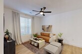Located at 10060 W Desert River Blvd in Glendale, AZ, this well-appointed one-bedroom, one-bathroom residence offers a thoughtfully designed single-floor layout. Light wood-style flooring flows throughout, creating a warm and cohesive aesthetic. The open-concept living area features crisp white walls, a ceiling fan with light fixture, and a large window that invites natural light. This space connects seamlessly to the dining area, which includes a glass door providing outdoor views, and to the kitchen. The kitchen is a standout feature, showcasing a large white quartz island with bar seating, matte black pendant lighting, stainless steel appliances, and a mix of white and navy cabinetry. The bedroom is a comfortable retreat highlighted by a sage green accent wall, a ceiling fan, and direct access to a walk-in closet with built-in shelving rods. Two additional closets provide generous storage throughout the unit. The bathroom features a navy vanity with gold hardware, a white quartz countertop, wood-look tile flooring, and a full soaking tub with tiled surround. A dedicated in-unit laundry area completes this efficient and stylish home.