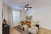 Located at 10060 W Desert River Blvd in Glendale, AZ, this well-appointed one-bedroom, one-bathroom residence offers a thoughtfully designed single-floor layout. Light wood-style flooring flows throughout, creating a warm and cohesive aesthetic. The open-concept living area features crisp white walls, a ceiling fan with light fixture, and a large window that invites natural light. This space connects seamlessly to the dining area, which includes a glass door providing outdoor views, and to the kitchen. The kitchen is a standout feature, showcasing a large white quartz island with bar seating, matte black pendant lighting, stainless steel appliances, and a mix of white and navy cabinetry. The bedroom is a comfortable retreat highlighted by a sage green accent wall, a ceiling fan, and direct access to a walk-in closet with built-in shelving rods. Two additional closets provide generous storage throughout the unit. The bathroom features a navy vanity with gold hardware, a white quartz countertop, wood-look tile flooring, and a full soaking tub with tiled surround. A dedicated in-unit laundry area completes this efficient and stylish home.