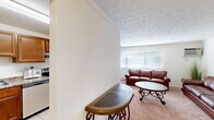 This single-floor, one-bedroom, one-bathroom residence offers a practical and comfortable layout across a compact yet efficient footprint. The combined living and dining area serves as the heart of the home, featuring soft wall-to-wall carpeting, a textured ceiling, and a wide window fitted with horizontal blinds that allows natural light to fill the space. A wall-mounted air conditioning unit provides climate control directly in the living area. The dining space accommodates a round wooden table with ample seating, seamlessly connected to the living room for easy everyday use.

The kitchen is a functional standout, featuring rich warm-toned cabinetry, granite-style countertops, light tile flooring, and stainless steel appliances including a full-size refrigerator, an electric range, and a sink with ample counter space on either side — well-suited for cooking and meal preparation.

The bedroom is a generously proportioned retreat with soft carpeting, a ceiling fan, and a louvered closet door providing convenient storage access.

The bathroom is clean and well-appointed, featuring tile flooring, white cabinetry with an integrated vanity, a mirrored medicine cabinet with overhead lighting, white tile wainscoting, and a shower/tub combination. A connecting hallway links all areas of the home efficiently, completing this thoughtfully arranged single-level residence.