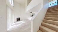Located at 3573 Columbia Ave in Riverside, CA, this two-story home offers a thoughtfully designed layout spread across two floors. The main level features an open-concept living room and kitchen area, where dramatic vaulted ceilings soar overhead, creating a striking sense of vertical space. Light wood-style flooring runs throughout the ground floor, reflecting abundant natural light that streams in through large windows and a sliding glass door. A classic fireplace serves as the focal point of the living room, adding warmth and character to the space. The kitchen is efficiently designed with white cabinetry, dark countertops, stainless steel appliances including a microwave and refrigerator, and recessed lighting set within a tray ceiling. A pass-through counter connects the kitchen to the living area. A full bathroom on this level features a tub-shower combination with sliding glass doors. Carpeted stairs lead to the upper floor, where the bedroom showcases its own vaulted ceiling, creating an airy and comfortable retreat. An en-suite bathroom on this level includes a vanity with white cabinetry and dark countertops. A closet completes the upper level. Throughout, the home features a clean, neutral palette of crisp white walls and light finishes.