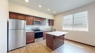 Located at 7112 265th St NW, Unit 316 in Stanwood, Washington, this efficiently designed single-floor unit offers a thoughtful layout that maximizes every square foot. The open kitchen serves as the centerpiece of the space, showcasing rich dark-walnut cabinetry, stone-look tile backsplash, white quartz-style countertops, and a full suite of stainless steel appliances including a refrigerator, electric range, built-in microwave, and dishwasher. A central kitchen island provides additional counter space and casual seating, enhancing the functionality of the room. Natural light filters in through a window overlooking the outdoors, brightening the kitchen and adjacent living area. Warm-toned luxury vinyl plank flooring runs throughout the unit, offering both durability and a cohesive aesthetic. The hallway connects the main living area to the bathroom, which is equipped with a stacked washer and dryer unit — a practical in-unit laundry solution — along with a vanity featuring matching dark cabinetry. Recessed lighting in the kitchen and clean, neutral wall tones throughout contribute to a bright, modern ambiance. A utility panel and closet are also conveniently accessible from the main living space, rounding out this functional and well-appointed unit.
