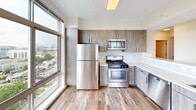 Located in Stamford, CT, this well-appointed 3-bedroom, 2-bathroom residence offers a thoughtfully designed single-floor layout with a generous overall footprint. The open-concept kitchen and living area serves as the heart of the home, showcasing warm wood-grain cabinetry, a marble-style quartz peninsula, and a full suite of stainless steel appliances including a gas range, microwave, and refrigerator. Large windows flood the kitchen with natural light and frame sweeping elevated views of the surrounding cityscape and waterway beyond. The living room features rich hardwood flooring and sliding glass doors that open directly onto a private balcony, extending the living space outdoors with striking panoramic views. Each of the three bedrooms continues the hardwood floor aesthetic and benefits from floor-to-ceiling windows that invite abundant natural light and showcase the vibrant urban surroundings. The generously sized primary bedroom offers particularly expansive proportions. The two bathrooms are finished in a clean, contemporary style with white vanities, tile flooring, large mirrors with vanity lighting, and walk-in shower enclosures. A dedicated entrance and closet complete the layout, providing practical storage solutions. The overall ambiance is modern, bright, and airy throughout.