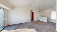 Located at 2864 Carpenter Rd in Ann Arbor, Michigan, this three-bedroom, two-bathroom residence offers a functional and well-organized single-floor layout. The living area is a standout space, featuring vaulted ceilings, plush carpeting, a wood-burning fireplace with a built-in mantel shelf, and a sliding glass door that opens to a private balcony, filling the room with abundant natural light. Adjacent to the living area, the combined dining and kitchen space features a pass-through counter with light-toned laminate surfaces, warm wood cabinetry, and white appliances including a range and refrigerator. The three bedrooms are carpeted and bright, each with windows that invite natural light; the primary bedroom is generously sized and includes closet access. Both bathrooms share a consistent design with vanity storage, large mirrors, a bathtub-shower combination, and distinctive tile flooring. One bathroom conveniently houses a stacked washer and dryer unit, integrating laundry into the layout. Throughout the home, clean white walls, multiple closets, and carpeted hallways contribute to a tidy, neutral interior. A carpeted staircase connects to additional levels of the building.