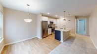 Located at 212 Bennington Hills Ct in West Henrietta, NY, this single-floor residence offers a thoughtfully designed layout with a clean, contemporary aesthetic throughout. The heart of the home is a well-equipped kitchen featuring crisp white cabinetry, gleaming granite countertops, and a large center island with a double-basin sink. Stainless steel appliances — including a refrigerator, electric range, and built-in microwave — complete the space, while pendant lighting and recessed fixtures create a warm, functional ambiance. The kitchen flows seamlessly into adjacent living areas, where light hardwood flooring transitions to plush, neutral-toned carpeting. Bedrooms are generously proportioned, each bathed in natural light through large windows dressed with white blinds, and finished with soft carpet underfoot. A spacious walk-in closet outfitted with multi-tiered wire shelving systems provides excellent storage and organization. The bathroom is finished with wood-toned cabinetry, granite countertops, a tub-shower combination, and hardwood-style flooring, with accessibility-friendly grab bars installed along the walls. Neutral warm beige tones carry throughout the entire residence, contributing to a cohesive and inviting atmosphere.