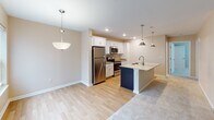 Located at 212 Bennington Hills Ct in West Henrietta, NY, this single-floor residence offers a thoughtfully designed layout with a clean, contemporary aesthetic throughout. The heart of the home is a well-equipped kitchen featuring crisp white cabinetry, gleaming granite countertops, and a large center island with a double-basin sink. Stainless steel appliances — including a refrigerator, electric range, and built-in microwave — complete the space, while pendant lighting and recessed fixtures create a warm, functional ambiance. The kitchen flows seamlessly into adjacent living areas, where light hardwood flooring transitions to plush, neutral-toned carpeting. Bedrooms are generously proportioned, each bathed in natural light through large windows dressed with white blinds, and finished with soft carpet underfoot. A spacious walk-in closet outfitted with multi-tiered wire shelving systems provides excellent storage and organization. The bathroom is finished with wood-toned cabinetry, granite countertops, a tub-shower combination, and hardwood-style flooring, with accessibility-friendly grab bars installed along the walls. Neutral warm beige tones carry throughout the entire residence, contributing to a cohesive and inviting atmosphere.