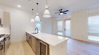 This single-floor unit showcases a clean, contemporary design throughout. The open-concept kitchen and living area serves as the heart of the space, anchored by a generously sized white quartz island with an undermount sink and matte black faucet. Three cone-shaped pendant lights hang above the island, while light wood cabinetry, a subway tile backsplash, and stainless steel appliances — including a refrigerator, microwave, and wine cooler — complete the kitchen. Light hardwood flooring flows seamlessly from the kitchen through the living area, which benefits from abundant natural light through tall windows and a glass-paneled door. A distinctive ceiling fan with blue blades adds a modern accent overhead.

The bedrooms continue the light, airy aesthetic with large windows, ceiling fans, and the same hardwood flooring. One bedroom features a glass door leading to an exterior exit. Two well-appointed bathrooms round out the unit: one features a glass-enclosed walk-in shower with marble-style tile surround and a sleek vanity with matte black hardware, while the second offers a soaking tub with a matching marble-tile surround. Both bathrooms feature large-format tile flooring and white quartz countertops, maintaining a cohesive, upscale finish throughout.