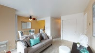 This single-floor residence offers a comfortable and functional layout across several well-defined living spaces. The living room is warm and inviting, featuring carpet flooring, a ceiling fan with light fixture, and a bold accent wall. A large sliding glass door floods the space with natural light and provides direct access to an outdoor area, while vertical blinds offer privacy and light control. The kitchen is efficiently designed with a galley-style layout, offering warm wood cabinetry, light countertops, wood-look flooring, and white appliances including a gas range and refrigerator — providing ample storage and workspace. The primary bedroom is generously sized, with plush carpet, a wall-mounted air conditioning unit, and a sliding glass door that opens to a private outdoor deck with views of surrounding greenery. A second bedroom offers versatility, with carpet flooring, a window with outdoor views, and enough space to function as a sleeping area or home office. The full bathroom is thoughtfully appointed with a tub-shower combo, neutral tile surround, a wood-toned vanity with integrated sink, and a well-lit mirror. Throughout the residence, neutral tones and natural light create a cohesive, welcoming ambiance.