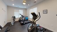 Located at 1710 Eighth Street Dr NE in Hickory, North Carolina, this dedicated fitness space is thoughtfully designed to support a full range of workout activities. The single-floor layout is finished with durable rubber flooring throughout, providing a safe and resilient surface suited for cardio, strength training, and stretching exercises.

The space is divided into two connected areas. The primary room features crisp white walls, recessed lighting, and a ceiling fan, creating a clean and well-lit environment. Multiple windows fitted with blinds allow natural light to filter in while maintaining privacy. A wall-mounted flat-screen television serves as a focal point for entertainment during workouts. Cardio equipment includes a Sole elliptical trainer, a Sole treadmill, and a stationary bike, while a set of dumbbells and a workout bench accommodate strength-focused training. A motivational "You Got This" wall decal adds an encouraging touch to the atmosphere.

An interior window connects the two areas, enhancing the sense of openness between them. The secondary room provides additional workout space and storage, with a door leading to an adjacent area. Natural light, organized equipment, and a practical layout make this fitness space functional and inviting for daily use.