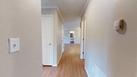 Located at 1405 SW Tenth St in Loveland, Colorado, this single-floor unit offers a straightforward, functional layout with a clean, neutral palette throughout. The open living and dining area is finished with warm wood-look flooring and accented by crown molding and a classic chandelier, creating an inviting atmosphere. The space flows naturally toward the kitchen, which features white cabinetry extending to the ceiling, light countertops, a double sink, and white appliances including a refrigerator, electric range, and dishwasher. A flush skylight fixture provides bright overhead illumination.

A hallway connects the main living areas to the bedrooms and bathrooms, lined with white-trimmed doors and consistent wood-look flooring. The bedrooms are carpeted with neutral tones and include closet storage. The primary bathroom features a vanity with ample cabinet storage, a large mirror with overhead lighting, and vaulted ceiling detail. A full bathroom accessible from the hallway includes a tub-shower combination, vanity, and wood-look flooring. A dedicated utility room houses the washer, water heater, and electrical panel, adding practical convenience to the unit's overall design.