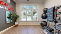 Located at 386 Attenborough Dr in Nottingham, MD, this single-room fitness studio is a thoughtfully designed space dedicated to functional training and wellness. The room features light wood-look flooring that lends a clean, modern aesthetic throughout. A striking accent wall in dark gray displays bold motivational signage — "Challenge Your Limits" — setting an energizing tone the moment you enter.

Large, multi-pane windows along one wall flood the space with abundant natural light and offer views of the lush outdoor greenery and pool area beyond, creating an inviting and airy atmosphere. Crown molding along the ceiling adds a refined architectural detail that elevates the overall finish of the room.

The studio is equipped with a SmartMat multi-station equipment rack stocked with stability balls, medicine balls, resistance bands, foam rollers, and kettlebells in varying weights, providing versatile options for strength and core training. A decorative fiddle-leaf fig plant adds a touch of organic warmth to the space.

Entry is through a frosted glass door that provides privacy while maintaining a sense of openness. A wall-mounted mirror and framed certifications complete the professional setup. This compact yet functional studio is ideal for personal training sessions or small group fitness classes.