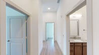 This contemporary single-floor residence is thoughtfully designed with a clean, modern aesthetic throughout. Light wood-tone flooring flows seamlessly from room to room, complementing the crisp white walls and creating a bright, cohesive atmosphere.

The open-concept kitchen serves as a central hub of the space, featuring rich dark wood cabinetry, stainless steel appliances, and a generous granite-topped island with a built-in sink. Pendant lighting accents the island, while floor-to-ceiling windows and glass doors flood the area with natural light and offer expansive outdoor views.

The hallway connects the living areas to the private rooms with ease, lined with recessed lighting overhead and clean architectural lines. Bedrooms are well-proportioned, each benefiting from windows that invite natural light and outdoor scenery.

The primary bathroom is a standout feature, offering both a soaking tub and a separate glass-enclosed walk-in shower, all finished with white subway tile and granite countertops atop dark wood vanity cabinetry. A second full bathroom mirrors the same design sensibility, with a glass-door shower and matching granite finishes.

Storage is well-addressed throughout, including a dedicated walk-in closet equipped with wire shelving systems. The overall ambiance of the space is clean, modern, and move-in ready.