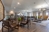This single-story community space in Alpharetta, Georgia, offers a well-appointed, open-concept layout designed for gathering and entertaining. The interior is finished with warm hardwood-style flooring throughout, white shiplap wall paneling, and crown molding that lend a clean, transitional aesthetic.

The kitchen is a standout feature, centered around a curved dark-cabinetry island with stainless steel countertops and a professional-grade faucet. Pendant globe lights in brushed metal hang above, while stainless steel appliances—including a full-size refrigerator and microwave—complete the functional setup. Large windows and French doors flood the space with natural light and provide views of the surrounding outdoor area.

Adjacent to the kitchen, the dining area accommodates a large rectangular table with seating for multiple guests, anchored by a striking black lantern-style chandelier. The lounge area features leather and upholstered seating arranged around a mirrored accent table, with a wall-mounted television and gallery-style framed artwork on the shiplap wall. A dedicated clubroom space off the lounge includes a large decorative Scrabble board, adding a playful, social touch to the overall ambiance.