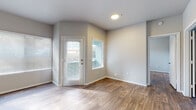 This single-floor residence offers a clean, modern aesthetic defined by consistent wood-look flooring, neutral gray walls, and white trim throughout. The open living area is bright and welcoming, featuring a ceiling fan, multiple windows with horizontal blinds, and a glass-panel door that invites abundant natural light and outdoor views of surrounding greenery. The kitchen is thoughtfully designed with rich dark-wood cabinetry, light quartz countertops, stainless steel appliances including a refrigerator, electric range, and built-in microwave, as well as a deep single-basin sink with a flexible-head faucet. The layout flows naturally into the living spaces, making it well-suited for both everyday living and entertaining. The bedrooms are generously sized, each featuring wood-look flooring, natural light from large windows, and ample wall space. The primary bathroom includes a dual-sink vanity with dark cabinetry and quartz countertops, a large mirror, and a full tub-shower combination with tile surround. A dedicated laundry area houses a full-size washer along with a water heater, complemented by wire shelving for additional storage. Overall, the space presents a cohesive, contemporary feel with practical amenities throughout.