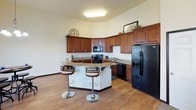 This two-floor residence offers a thoughtfully designed layout that balances functionality and comfort throughout. The kitchen serves as a central highlight, showcasing rich dark-stained cabinetry with ample storage, granite countertops, black appliances including a range, dishwasher, and refrigerator, and a peninsula with seating — all set atop warm hardwood-style flooring. The open living area is bathed in natural light courtesy of large, dark-framed windows with transom panels above, offering views of the surrounding neighborhood and creating an airy, welcoming atmosphere. Neutral-toned walls and plush carpeting run throughout the residential areas, contributing to a clean and cohesive aesthetic. Multiple bedrooms provide comfortable retreats, each carpeted and featuring windows that bring in natural light, with ample space for furniture. The bathrooms are well-equipped, including a unit with a walk-in shower stall with grab bar and another with a vanity featuring granite countertops, wood cabinetry, and a tub-shower combination. A carpeted staircase connects the two floors, with an additional versatile room offering flexible use as a bedroom or office. The overall design is practical and move-in ready.