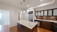 Located at Metropolitan 11 in Memphis, TN, this well-appointed three-bedroom, two-bathroom residence offers a thoughtfully designed single-floor layout with a clean, modern aesthetic throughout. The kitchen serves as a centerpiece, showcasing a large granite-topped island beneath stylish pendant lighting, dark espresso cabinetry with frosted glass upper panels, a warm tile backsplash, and a full suite of stainless steel appliances including a French door refrigerator, dishwasher, microwave, and range. The living areas feature rich hardwood flooring that reflects natural light streaming in through multiple windows fitted with blinds. The spacious primary bedroom includes plush carpeting, a ceiling fan, and closet access. Additional bedrooms also offer hardwood floors and generous natural light. The primary bathroom is equipped with both a soaking tub and a separate glass-enclosed shower, set against neutral tile surrounds, while the second bathroom features a granite vanity with dark wood cabinetry and tile flooring. Two hallways and two closets contribute to practical storage and circulation. The overall palette of whites, warm woods, and stone tones creates a cohesive, contemporary living environment.