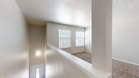 This single-floor residence offers a practical and well-organized layout encompassing two bedrooms, one bathroom, a kitchen, hallway, and staircase. The entry staircase leads to the main living level, where neutral-toned walls, textured ceilings, and wall-to-wall carpeting create a consistent and understated aesthetic throughout the living and sleeping areas.

The galley-style kitchen is efficiently designed with white upper cabinetry, gray lower cabinets, white subway tile backsplash, light-tiled flooring, and white countertops. Black appliances, including a refrigerator, electric range, microwave, and dishwasher, provide a functional contrast to the bright cabinetry.

Both bedrooms feature soft carpeting and white horizontal blinds that allow natural light to filter in. The primary bedroom includes a ceiling fan with integrated lighting, while the secondary bedroom offers a similarly bright, carpeted space. The hallway area contains an electrical panel accessible from the carpeted corridor.

The bathroom is finished with large-format tile flooring, a full tub-shower combination, a gray vanity with white countertop, overhead cabinetry, and a lighted mirror, providing a clean and practical design.