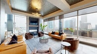 Located in the heart of Charlotte, NC, this expansive, single-floor amenity space at 500 W Trade St offers a refined blend of modern design and urban sophistication. The layout encompasses two well-appointed kitchen and living areas, each with its own distinct character, plus a generous outdoor balcony.

The first kitchen and living area is anchored by a dramatic oversized island with a sleek stone countertop, detailed mosaic tile accents, and a row of sculptural barrel-style bar seating. Pendant lighting, textured tile backsplash, and stainless steel appliances lend a polished, upscale feel. This space flows into a lounge area with a coffered, richly patterned ceiling, herringbone wood flooring, and floor-to-ceiling windows framing breathtaking Charlotte skyline views.

The second kitchen and living area features bold globe chandeliers with brass detailing, mixed stone and wood flooring, and another generously sized island beneath pendant lights. Large windows flood the space with natural light and connect seamlessly to the balcony, where glass railings reveal sweeping panoramic views of the city and surrounding landscape.

Throughout, the design integrates warm leather furnishings, statement lighting, lush indoor plants, and high-end finishes, creating an inviting yet sophisticated atmosphere ideal for gathering and entertaining.