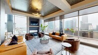 Located in the heart of Charlotte, NC, this expansive, single-floor amenity space at 500 W Trade St offers a refined blend of modern design and urban sophistication. The layout encompasses two well-appointed kitchen and living areas, each with its own distinct character, plus a generous outdoor balcony.

The first kitchen and living area is anchored by a dramatic oversized island with a sleek stone countertop, detailed mosaic tile accents, and a row of sculptural barrel-style bar seating. Pendant lighting, textured tile backsplash, and stainless steel appliances lend a polished, upscale feel. This space flows into a lounge area with a coffered, richly patterned ceiling, herringbone wood flooring, and floor-to-ceiling windows framing breathtaking Charlotte skyline views.

The second kitchen and living area features bold globe chandeliers with brass detailing, mixed stone and wood flooring, and another generously sized island beneath pendant lights. Large windows flood the space with natural light and connect seamlessly to the balcony, where glass railings reveal sweeping panoramic views of the city and surrounding landscape.

Throughout, the design integrates warm leather furnishings, statement lighting, lush indoor plants, and high-end finishes, creating an inviting yet sophisticated atmosphere ideal for gathering and entertaining.