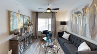 This thoughtfully designed single-floor residence combines modern aesthetics with functional living. The kitchen is a standout feature, showcasing dark espresso cabinetry that extends to the ceiling, bright white quartz countertops, a subway tile backsplash, and a full suite of stainless steel appliances including a refrigerator, range, microwave, and dishwasher. A central island with bar seating provides additional prep space and casual dining. Light wood-style flooring flows throughout the main living areas, lending warmth and continuity to the space. The living room offers a comfortable, open layout with a large window that draws in natural light, complemented by a ceiling fan overhead. The bedroom is generously sized, featuring plush carpeting, a ceiling fan, natural light from a window with blinds and drapery, and direct access to a spacious walk-in closet with ample hanging and storage space. The bathroom is clean and contemporary, finished with tile flooring, a tub-shower combination with a tile surround, and neutral wall tones. An in-unit laundry area adds a practical convenience. Throughout, the space maintains a cohesive, modern palette of whites, grays, and warm wood tones, creating an inviting and polished atmosphere.