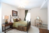 This single-story residence offers a thoughtfully designed layout across multiple rooms, each finished with practical details and a warm aesthetic. The living room features crown molding, a ceiling fan with light fixture, and large windows dressed with warm-toned curtains that allow generous natural light. A large armoire anchors one side of the room, while the seating area provides a comfortable and well-defined space for relaxing.

The kitchen is outfitted with white cabinetry, dark countertops, tile flooring, and recessed lighting. A peninsula with bar seating adds functionality, while a window above the sink brings in additional natural light. Full appliances, including a refrigerator, range, microwave, and dishwasher, are included.

The dining area accommodates a round wood table and features a window, providing a pleasant setting for meals. The bedroom is carpeted and well-proportioned, featuring a ceiling fan, a window with drape treatments, and access to a walk-in closet and an en-suite vanity area. The full bathroom includes a single-sink vanity with dark countertop, white cabinetry, and a tub-shower combination with sliding glass doors over tile flooring. A dedicated laundry room with a full-size washer and dryer, overhead cabinetry, and built-in shelving completes the home.