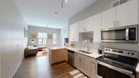 This thoughtfully designed single-floor residence offers three bedrooms and three full bathrooms, making efficient use of its well-organized layout. The open-concept kitchen and living area serves as the heart of the home, where a sleek, modern kitchen features two-tone cabinetry — crisp white upper cabinets paired with warm wood-toned lower cabinets — complemented by white quartz countertops and a full suite of stainless steel appliances, including a refrigerator, range, microwave, and dishwasher. Rich wood-look flooring runs throughout the main living area, adding warmth and continuity. The adjacent living room benefits from multiple windows that invite natural light, while elevated ceilings with track lighting contribute to an airy, open ambiance. Each bedroom is carpeted for comfort and includes a window for natural light and closet storage, with the rooms offering a cozy yet functional scale ideal for a desk and sleeping area. The three bathrooms are finished consistently with light wood vanities, white quartz countertops, undermount sinks, and wood-look flooring, maintaining a clean, cohesive aesthetic. Neutral wall tones throughout the residence create a calm, contemporary atmosphere well-suited for modern living.