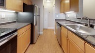 This single-floor residence is thoughtfully laid out to maximize functionality across its living spaces. The galley-style kitchen is efficiently designed with warm honey-toned cabinetry lining both walls, dark speckled countertops, and a gray subway tile backsplash. Stainless steel appliances, including a refrigerator and dishwasher, complement the space, while durable wood-look flooring runs the length of the kitchen toward a hallway closet beyond.

The living area is generously proportioned, featuring neutral-toned wall-to-wall carpeting, soft beige walls, and a ceiling fan with light fixture. An arched architectural detail connects the kitchen pass-through to the living space, adding a subtle design element. A large window with vertical blinds allows natural light to fill the room.

The bedroom offers comfortable carpeted flooring, a window with blinds, and a closet. Neutral walls and clean white baseboards maintain a consistent, understated aesthetic throughout. An additional room provides similar finishes with natural light from a window.

The bathroom includes a full-size soaking tub with a tub/shower combination, chrome fixtures, and clean white surroundings, keeping the space bright and functional.