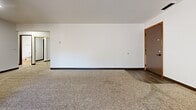 Located at 201 E Arbor Ave in Bismarck, North Dakota, this two-bedroom, one-bathroom unit offers a well-organized single-floor layout with a comfortable and functional living environment. The living area is generously sized, featuring plush carpet, a textured ceiling, and a sliding glass door that opens onto a private balcony overlooking mature trees — bringing in natural light and outdoor views. The kitchen is laid out in a practical galley style with warm honey-toned wood cabinetry, ample counter space, vinyl plank flooring, and a full suite of white appliances including a refrigerator, range, and dishwasher, along with a window for natural light. The primary bedroom is notably spacious, offering room for large furniture, a ceiling fan with light fixture, a window with outdoor views, and direct access to a generous walk-in closet with built-in rod and shelving. The second bedroom is bright and carpeted with its own window and closet access. The bathroom features a clean, white tub-shower combo with hardwood-style flooring and adjacent open shelving. Throughout the unit, dark wood trim and warm-toned interior doors provide consistent character, while the hallway connects all rooms with ease.
