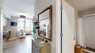 Located at 26 University Place Blvd in Jersey City, NJ, this thoughtfully designed studio unit makes excellent use of its compact footprint across a single floor. The open-concept kitchen and living area serves as the heart of the unit, featuring light wood-style flooring, neutral tones, and a window that brings in natural light with outward-facing views. The kitchen is well-appointed with stainless steel appliances — including a range, microwave, refrigerator, and dishwasher — complemented by two-tone cabinetry with white upper cabinets and dark lower cabinets, a white subway tile backsplash, and clean white countertops. The living area offers flexible space for both relaxation and a home workspace. A welcoming hallway connects the main living space to the rest of the unit, and a decorative mirror and storage dresser add functional character near the entry. The bathroom features large-format tile flooring and a subway-tiled walk-in shower with a glass enclosure. Three closets provide generous storage throughout, and a dedicated in-unit laundry area adds everyday convenience. This unit offers a modern, efficient layout suited for comfortable urban living in Jersey City.