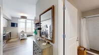 Located at 26 University Place Blvd in Jersey City, NJ, this thoughtfully designed studio unit makes excellent use of its compact footprint across a single floor. The open-concept kitchen and living area serves as the heart of the unit, featuring light wood-style flooring, neutral tones, and a window that brings in natural light with outward-facing views. The kitchen is well-appointed with stainless steel appliances — including a range, microwave, refrigerator, and dishwasher — complemented by two-tone cabinetry with white upper cabinets and dark lower cabinets, a white subway tile backsplash, and clean white countertops. The living area offers flexible space for both relaxation and a home workspace. A welcoming hallway connects the main living space to the rest of the unit, and a decorative mirror and storage dresser add functional character near the entry. The bathroom features large-format tile flooring and a subway-tiled walk-in shower with a glass enclosure. Three closets provide generous storage throughout, and a dedicated in-unit laundry area adds everyday convenience. This unit offers a modern, efficient layout suited for comfortable urban living in Jersey City.