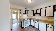 Partridge Meadows Apartments is a two-story residential unit designed with everyday functionality in mind. The kitchen serves as a practical hub of the home, featuring white cabinetry accented with dark brown trim, offering ample storage through a combination of upper and lower cabinets. The countertops provide generous workspace, and the kitchen is equipped with a white electric range and a dishwasher, making meal preparation and cleanup convenient. A double-basin sink sits beneath an open layout that connects seamlessly to the adjacent living area, allowing for an easy flow between spaces. The flooring in the kitchen features a durable tile pattern, while the living area transitions to carpet, adding warmth underfoot. Natural light filters into the living space through sliding glass doors or large windows, brightening the interior. The textured ceiling and centrally mounted light fixtures are consistent throughout, contributing to a cohesive and straightforward aesthetic. A visible hallway connects the main living areas to additional rooms across the two floors, providing a practical and navigable layout. Overall, Partridge Meadows Apartments presents a clean, functional living environment well-suited for comfortable everyday living.