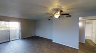 This single-floor space presents a well-maintained and functional layout with a consistent design aesthetic throughout. The main living area is immediately welcoming, showcasing rich, dark hardwood flooring that extends across the entire space, providing warmth and a polished finish underfoot. Neutral gray walls create a clean, versatile backdrop suited to a variety of décor styles.

A ceiling fan with an integrated light fixture is centrally mounted, ensuring year-round comfort and adequate lighting. The living area is generously sized and benefits from abundant natural light, courtesy of large windows fitted with horizontal blinds that offer adjustable privacy and light control.

A fireplace serves as a notable architectural focal point within the main living area, adding both character and a cozy ambiance to the space. Sliding glass doors, framed by vertical blinds, provide direct access to an outdoor area while drawing in additional natural light and views of the exterior surroundings.

The space also features multiple air vents integrated into the ceiling, indicating a central HVAC system for efficient climate control. Clean white baseboards frame each room, adding a crisp finishing touch. Overall, the space combines practical features with a neutral, move-in-ready aesthetic that offers both comfort and versatility.
