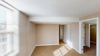 This single-floor residence offers a practical and straightforward layout with distinct living, sleeping, and functional zones. The living area is generously sized, finished with neutral-toned carpet and beige walls beneath a textured ceiling. Natural light filters in through blinded windows, lending the space a bright, open feel. A ceiling fan serves the adjacent area near the kitchen, providing both comfort and airflow.

The kitchen is equipped with warm honey-toned wood cabinetry arranged in an L-shape, offering ample upper and lower storage. Light-toned countertops, a stainless double-basin sink, a black gas range, and a full-size black refrigerator complete the functional setup. Stone-look vinyl flooring ties the kitchen together cleanly.

The bedrooms feature wall-to-wall carpet and neutral paint tones. One bedroom benefits from dual closets side by side, each fitted with hanging rods and shelving, providing notable storage capacity. Another carpeted room features two windows that bring in plentiful natural light.

The bathroom includes a full-size soaking tub and shower combination with a white surround and a curved curtain rod. White trim and baseboards are consistent throughout, contributing to a cohesive, clean aesthetic across the entire space.