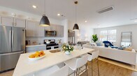 Located at 100 Woodside Court in Trumbull, Connecticut, this two-story townhouse offers a thoughtfully designed layout across two floors. The entry foyer welcomes residents with light wood-style flooring, a striped area rug, and a warm wood staircase with a classic handrail leading to the upper level.

The main floor showcases an open-concept kitchen and living area that is both functional and stylish. The kitchen is outfitted with gray shaker-style cabinetry, white quartz countertops, a white subway tile backsplash, and a full suite of stainless steel appliances including a gas range, microwave, and French door refrigerator. A central island with pendant lighting and bar seating flows seamlessly into the dining and living areas. The living room benefits from large windows that invite abundant natural light and features neutral tones complemented by tasteful décor. A convenient half bath completes the main level.

Upstairs, two well-proportioned bedrooms each feature plush carpeting and large windows with views of the surrounding neighborhood. The primary bedroom is served by a private en-suite bathroom with a shaker-style vanity, white quartz countertop, gold-toned hardware, and a glass-enclosed subway tile shower. A second full bathroom with a tub-shower combination serves the additional bedroom and guests.