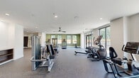 Located at 523 Chestnut Ave in Woodbury Heights, NJ, this single-floor fitness center offers a generously sized, thoughtfully designed exercise space built to accommodate a full range of workout needs. The open layout is organized into distinct functional zones, flowing seamlessly from one area to the next across durable, rubber-composite flooring throughout.

The cardio zone is highlighted by floor-to-ceiling sliding glass doors and expansive windows that flood the space with natural light and provide open views of the surrounding community. Treadmills, ellipticals, stationary bikes, and a rowing machine are positioned to take full advantage of these outdoor sightlines. Ceiling fans overhead contribute to a comfortable workout environment.

The strength training area features a multi-station cable machine, a dedicated free weight section with a full rack of dumbbells, weight benches, and a mirrored accent wall that visually expands the space. Stability balls and additional functional fitness accessories are neatly arranged nearby.

A standout design detail is the built-in hydration station, framed by a striking blue ceramic tile accent wall, providing both a practical amenity and a bold visual focal point. Recessed lighting throughout ensures consistent, even illumination. The clean white walls, accented by sage green paint in select areas, give the space a modern and energizing aesthetic.