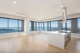 This contemporary high-rise residence is defined by its clean modern aesthetic and expansive floor-to-ceiling windows that frame panoramic views of the cityscape and waterfront beyond. Light wood flooring flows throughout the open living areas, enhancing the sense of space and continuity.

The kitchen is a standout feature, anchored by a large island with a quartz waterfall countertop and integrated gas cooktop beneath a ceiling-mounted stainless steel range hood. Dark wood-grain cabinetry lines the walls, complemented by premium stainless steel appliances including a French door refrigerator, double wall ovens, and a built-in microwave. The kitchen opens seamlessly into a generous living area bathed in natural light.

The primary bathroom is spa-inspired, featuring a freestanding soaking tub, a glass-enclosed walk-in shower, large-format tile flooring, and a floating double vanity topped by a backlit mirror. A secondary bathroom offers a glass-enclosed shower and floating vanity in a similarly refined finish.

Additional highlights include a dedicated walk-in closet with custom dark wood shelving and hanging systems, a built-in shelving unit in one of the living areas, and an in-unit laundry room equipped with a full-size Whirlpool washer and dryer.