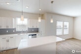 Located at 9000 Little Palm Way in Venice, FL, this thoughtfully designed two-story home offers a bright, modern interior spread across two floors. The ground floor is anchored by an open-concept kitchen and combined dining and living area, ideal for everyday living and entertaining. The kitchen is a standout feature, showcasing crisp white shaker cabinetry, a grey subway tile backsplash, gleaming quartz countertops, a central island, and stainless steel appliances including a range, microwave, dishwasher, and refrigerator. Three pendant lights hang above the space, complementing the vaulted ceiling and multiple windows that flood the area with natural light. Light wood-style flooring runs throughout, adding warmth to the clean, neutral palette. The entrance provides a welcoming transition into the home, with staircase access leading to the upper floor. Upstairs, the generously sized primary bedroom features dual windows and a ceiling fan, while two closets offer ample storage. The full bathroom includes a large vanity with quartz countertop and a wide mirror. A dedicated laundry room houses a full-size washer and dryer. Outside, a private fenced yard with lush turf and a white vinyl privacy fence creates a serene outdoor retreat, accented by Florida-style landscaping.
