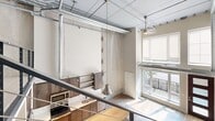 Located on Hennepin Avenue in the heart of Minneapolis, this two-story loft-style residence blends industrial character with modern comfort. The main floor welcomes you with light hardwood flooring, pendant lighting, and large windows that flood the space with natural light and offer views of the surrounding urban streetscape. A well-appointed kitchen features wood cabinetry, subway tile backsplash, and stainless steel appliances, while exposed ductwork and high ceilings reinforce the loft's industrial aesthetic. A striking open-riser staircase with a dark steel frame and wood treads, paired with sleek cable railings, serves as both a functional and architectural focal point connecting the two floors. The upper level features plush carpeting, exposed steel beam ceilings, and ductwork that continues the industrial theme, along with a walk-in closet offering built-in shelving. The full bathroom is finished with warm wood vanity cabinetry, a framed mirror, and a classic subway tile shower-tub combination. A dedicated laundry area with a stacked washer and dryer adds everyday convenience. With two staircases, a hallway, and additional closet storage, this loft delivers a thoughtfully functional layout ideal for urban living.