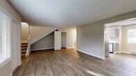 This two-story home offers a practical and well-organized layout across two floors. The main level features an open living room with durable wood-look plank flooring, neutral-toned walls, and a front-facing window that fills the space with natural light. A white-railed staircase leads to the upper level, while a convenient storage closet is tucked beneath the stairs. The kitchen is thoughtfully designed with gray cabinetry, white quartz-style countertops, stainless steel appliances including a dishwasher and refrigerator, and a ceiling fan overhead. Light wood-look flooring and a window overlooking the outdoors complete the kitchen's clean, functional aesthetic. Three bathrooms are distributed throughout the home, with at least one featuring a soaking tub, a vanity with a speckled countertop, a wall mirror, and a natural light-admitting window. The upper floor hosts both bedrooms, each carpeted for comfort and equipped with baseboard heating and windows with outdoor views. The spacious primary bedroom includes a dedicated bathroom and closet access. Hallways connect the rooms seamlessly on both levels. Throughout, textured ceilings, crisp white trim, and a cohesive neutral palette create a clean and move-in-ready atmosphere.