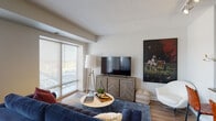 This single-floor residence offers a thoughtfully designed layout that balances functionality and comfort. The entryway corridor, accented by warm wall sconces and textured ceilings, leads into the main living area where large windows and a sliding glass door flood the space with natural light and provide views of the surrounding exterior. The living room features durable hardwood-style flooring, ample room for seating, and direct access to a private balcony.

The galley-style kitchen is efficiently designed with gray cabinetry, dark granite countertops, a stainless steel refrigerator, and a double sink — providing generous counter and storage space throughout. It opens conveniently toward the living and dining areas, promoting an easy flow for everyday use.

The bedroom is a calm, carpeted retreat with soft neutral tones, a textured ceiling, and closet storage. It offers a quiet atmosphere well-suited for rest. The bathroom is clean and bright, featuring a white vanity with under-cabinet storage, a large mirror with overhead lighting, hardwood-style flooring, and a shower-tub combination. Throughout the residence, a consistent neutral color palette, modern finishes, and practical design choices come together to create a cohesive and comfortable living environment.