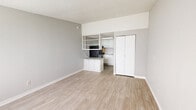 Located at 1500 Monument Rd in Jacksonville, Florida, this single-floor studio unit offers a practical and efficiently designed living space. The open-concept main area features light wood-tone laminate flooring throughout, neutral gray walls, and a textured ceiling, creating a clean and cohesive aesthetic.

The living area is bright and open, with a window fitted with blinds allowing natural light to filter in, complemented by a wall-mounted HVAC unit for year-round climate control. A white panel entry door provides direct access to the unit.

The kitchenette is thoughtfully integrated into the space, separated by a partial knee wall with white cabinetry and a granite-style countertop that doubles as a functional workspace or breakfast bar. Open wall-mounted shelving above houses a microwave, while the kitchen proper features white upper and lower cabinets, a sink, and a black refrigerator, all finished with a textured ceiling overhead.

A full-height double-door closet provides dedicated storage, keeping the main living area uncluttered. The bathroom includes wood-look flooring consistent with the rest of the unit, a vanity with granite-style countertop, toilet, and grab bars, reflecting a functional and accessible design. Overall, this studio presents a tidy, move-in-ready layout suited for practical, efficient living.