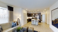 Located at 6963 E 109th Ave in Westminster, Colorado, this single-floor residence offers a thoughtfully designed open-concept layout that seamlessly connects the living and kitchen areas. The kitchen is a standout feature, showcasing dark espresso cabinetry that extends to the ceiling, stainless steel appliances including a refrigerator, microwave, and range, as well as a central island with seating for two, illuminated by sleek pendant lighting. Light wood-style flooring runs throughout the space, complementing the bright white walls and recessed lighting overhead to create a clean, airy atmosphere. The living area provides a comfortable and inviting setting, with ample room for seating arrangements. The open sightlines between rooms enhance the sense of spaciousness, making the home feel expansive and welcoming. The neutral color palette and modern finishes give the space a contemporary aesthetic that is both functional and visually appealing. Additional doors visible from the main living area suggest access to private rooms and storage, rounding out this well-appointed Westminster residence.