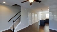 This two-story home offers a well-designed open floor plan that promotes a natural flow between living spaces. The main level is anchored by rich, dark hardwood flooring that extends throughout, providing a warm and grounded aesthetic. The open-concept layout connects the main living area directly to the kitchen, which features striking navy blue cabinetry, pendant lighting, and a functional sink island — a standout element that adds both style and practicality to the space.

The staircase, positioned prominently along one wall, features a classic dark wood handrail paired with sleek metal balusters, offering a refined transitional detail between the two floors. Neutral gray walls and white trim throughout create a clean, versatile backdrop that complements the darker flooring and cabinetry. A ceiling fan overhead provides both comfort and a touch of casual elegance to the main living area.

Multiple paneled interior doors line the hallway, suggesting well-defined storage or utility spaces that contribute to the home's organizational functionality. The upper level, accessible via the staircase, expands the overall living space further. The combination of thoughtful architectural details, a cohesive color palette, and quality finishes throughout gives this home a polished yet approachable character.
