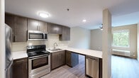 This single-floor, two-bedroom, one-bathroom unit in Lexington, Kentucky, offers a thoughtfully designed layout that maximizes its compact footprint. The open-concept kitchen and living area serves as the heart of the unit, where a well-appointed kitchen features dark espresso cabinetry, white countertops, and a full suite of stainless steel appliances, including a range, microwave, refrigerator, and dishwasher. A peninsula counter extends the workspace and creates a natural division between the kitchen and living area. Wood-style laminate flooring runs consistently throughout the unit, lending a cohesive, modern aesthetic.

Both bedrooms are comfortably proportioned, each equipped with a ceiling fan with integrated lighting. The primary bedroom is notably spacious, offering a large window with tree-lined outdoor views, filling the room with natural light. The second bedroom also features a window with greenery views. Neutral, warm-toned walls complement the flooring in both rooms.

The single bathroom is well-equipped with a dark-finished vanity, white countertop, a large mirror, and an accessible walk-in shower fitted with safety grab bars. Wood-style flooring continues here, maintaining design consistency. A hallway connects all rooms, completing this efficient and modern layout.
