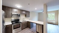 This single-floor, two-bedroom, one-bathroom unit in Lexington, Kentucky, offers a thoughtfully designed layout that maximizes its compact footprint. The open-concept kitchen and living area serves as the heart of the unit, where a well-appointed kitchen features dark espresso cabinetry, white countertops, and a full suite of stainless steel appliances, including a range, microwave, refrigerator, and dishwasher. A peninsula counter extends the workspace and creates a natural division between the kitchen and living area. Wood-style laminate flooring runs consistently throughout the unit, lending a cohesive, modern aesthetic.

Both bedrooms are comfortably proportioned, each equipped with a ceiling fan with integrated lighting. The primary bedroom is notably spacious, offering a large window with tree-lined outdoor views, filling the room with natural light. The second bedroom also features a window with greenery views. Neutral, warm-toned walls complement the flooring in both rooms.

The single bathroom is well-equipped with a dark-finished vanity, white countertop, a large mirror, and an accessible walk-in shower fitted with safety grab bars. Wood-style flooring continues here, maintaining design consistency. A hallway connects all rooms, completing this efficient and modern layout.