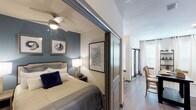 This single-floor residence offers a thoughtfully designed layout that balances style and functionality throughout. The bedroom is a standout feature, characterized by a rich steel-blue accent wall, soft carpeted flooring, a ceiling fan, and warm bedside lighting that creates a cozy, restful atmosphere. A sleek sliding door system separates the bedroom from the main living area, providing both privacy and an open, flexible feel when desired. Framed artwork adorns the walls, adding a curated aesthetic to the space.

The kitchen is outfitted with modern stainless steel appliances, including a full-size refrigerator, electric range, over-the-range microwave, and dishwasher. White cabinetry extends to the ceiling for ample storage, while light granite countertops and a subtle tile backsplash lend a clean, contemporary look. Light wood-style flooring runs through the main living areas, complementing the bright, neutral palette.

The bathroom is finished with white cabinetry, a single vanity with a wide mirror, and wood-look tile flooring. A full tub and shower combination with a curtain provides practical convenience, while decorative wall accents add a touch of personality. Natural light filters through window treatments in multiple rooms, contributing to the overall bright and inviting ambiance of this well-designed residence.