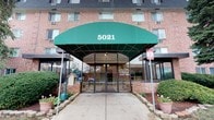 5021 is a multi-story brick residential building that presents a polished and well-maintained appearance. The building's most distinctive exterior feature is its prominent green fabric entrance canopy, which shelters the main entry and adds a welcoming character to the facade. The entrance is framed by glass doors and a concrete walkway, flanked by decorative planters that add subtle greenery to the approach.

The exterior is constructed of classic red brick, lending the building a solid and timeless aesthetic. Windows are evenly distributed across the facade, providing natural light to the individual units within. The building is managed by Equity Property Management, LLC, which offers 1 and 2 bedroom residences, as indicated by signage at the entrance.

The single-floor layout of the space captured in this tour offers a focused and accessible experience. The overall ambiance of the building conveys a sense of established, community-oriented residential living, with a neat and orderly exterior that reflects attentive property management. The landscaping at the entrance, including potted flowers and trimmed greenery, contributes to a tidy and inviting curb appeal that sets a welcoming tone for residents and visitors alike.