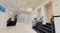 The Ponciana lobby presents a refined and elegantly designed entrance space that immediately establishes a sense of upscale hospitality. The flooring is finished in large-format polished marble tiles in a crisp white tone, contributing to the bright and airy atmosphere that defines the space. A coffered ceiling with recessed lighting serves as a sophisticated architectural detail overhead, while a statement crystal chandelier suspended from its center adds a glamorous focal point that enhances the overall grandeur.

A prominently positioned reception desk, clad in intricate mosaic tile detailing, displays the "Ponciana" name in illuminated lettering, functioning as both a practical and decorative centerpiece. To the right, a staircase with dark treads and ornately crafted wrought iron railings featuring scrollwork detailing adds a classical, European-inspired elegance. The walls are finished in crisp white with clean panel molding, reinforcing the formal aesthetic throughout.

An arched doorway visible in the background adds architectural depth and continuity, while additional lighting fixtures further illuminate the space. The overall ambiance is polished, welcoming, and meticulously curated to reflect a sophisticated design sensibility.