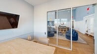 This 270 square foot studio apartment, located at 1050 S Babcock St in Melbourne, FL, showcases a thoughtful design that maximizes its compact footprint. The space is characterized by clean lines, neutral tones, and an abundance of natural light, creating an airy and inviting atmosphere.

The apartment features a versatile open-plan layout, seamlessly integrating the bedroom and living areas. Large windows with horizontal blinds allow ample daylight to flood the space, while offering privacy control. The flooring throughout is a warm, honey-toned hardwood in a herringbone pattern, adding visual interest and a touch of sophistication.

A glass partition wall separates the main living area from what appears to be a small dining or work nook, maintaining an open feel while defining distinct functional zones. The living area is furnished with comfortable blue armchairs and a round coffee table, all resting on a light-colored area rug.

The walls are painted in a crisp white, with a subtle two-tone effect created by a chair rail, adding depth to the room. Carefully chosen artwork adorns the walls, including a large, atmospheric landscape print that contributes to the space's serene ambiance.

Despite its limited square footage, the apartment appears to offer ample storage solutions, though these are not directly visible in the provided images. The overall design ethos focuses on functionality and style, creating a modern and efficient living space ideal for urban dwellers or those seeking a minimalist lifestyle.