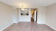 This two-story residence is thoughtfully designed across two levels, with living spaces on the lower floor and bedrooms situated upstairs. The entry level features a hallway with textured walls and light wood-look flooring that extends throughout the main living areas. A spacious living room anchors the lower level, enhanced by a pendant light fixture and a sliding glass door that fills the room with natural light and provides outdoor access.

The kitchen is positioned behind a pass-through opening that overlooks the living area, creating a connected and functional layout. It features white shaker-style cabinetry with matte black hardware, granite-look countertops, a stone tile backsplash, and black appliances, including an electric range and refrigerator. A half bathroom on the lower level offers a white vanity with a mirror and a natural light source from a side window.

Upstairs, the bedrooms are carpeted and feature ceiling fans, multiple windows, and sliding closet doors with built-in shelving. The upper-level full bathroom includes a granite-topped vanity with dual sconce lighting and a mirror, paired with wood-look tile flooring. A staircase with a classic railing connects both floors, completing the functional two-level layout.